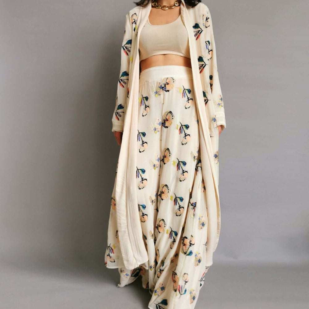 A model in a cream and white floral trousers and jacket posing elegantly for a photoshoot.