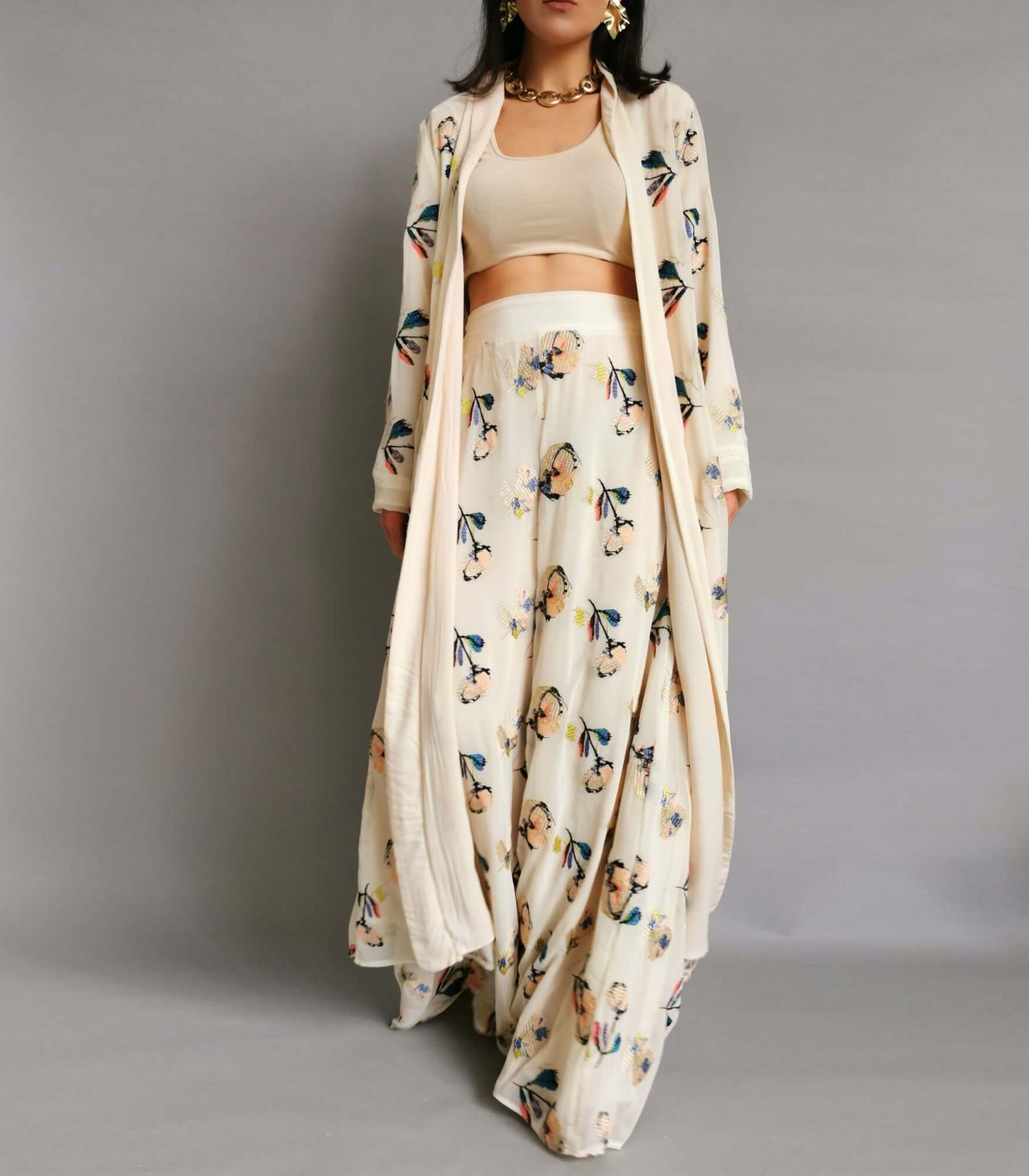 A model in a cream and white floral trousers and jacket posing elegantly for a photoshoot.