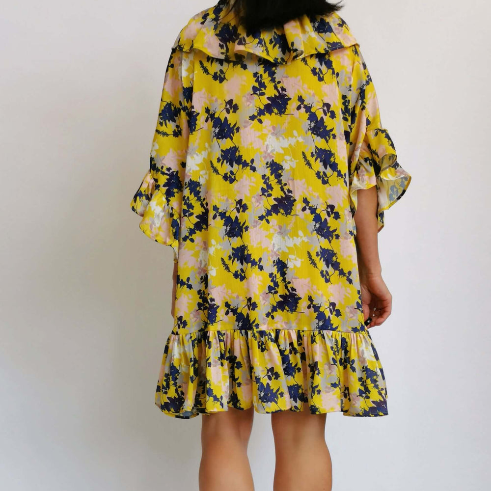 
                      
                        An elegant woman in a yellow floral dress, surrounded by flowers.
                      
                    