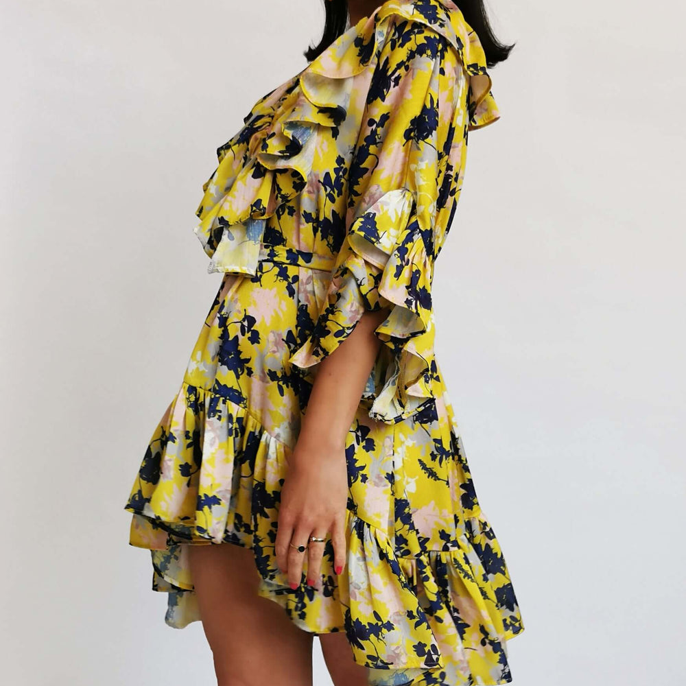 
                      
                        A lady in a bright yellow floral dress posing for a photo.
                      
                    